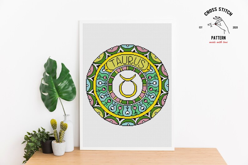 Peut inclure: Mod&egrave;le de point de croix pour une mandala color&eacute;e avec le signe du zodiaque Taureau au centre. La mandala est entour&eacute;e d'une bordure jaune avec le mot "Taureau" &eacute;crit en lettres jaunes.