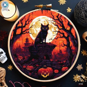 May include: A Halloween-themed cross-stitch design in a wooden hoop. The design features a black cat perched on a rooftop, with a full moon in the background. Pumpkins and a spooky town complete the scene, with a color palette of orange, black, and yellow.