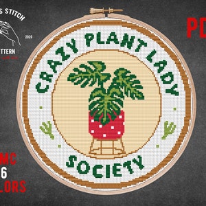 May include: A cross stitch pattern for a round embroidery hoop with the text "Crazy Plant Lady Society" in brown lettering. The design features a green monstera plant in a red and white polka dot pot. The pattern is available as a PDF download.