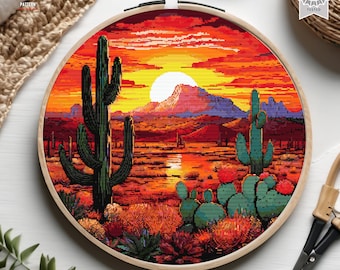 Può includere: Uno schema di punto croce che rappresenta un tramonto nel deserto con un grande cactus in primo piano e montagne sullo sfondo. Il cielo è di un arancione e rosso vibrante, con un sole giallo brillante.