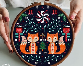 May include: Cross stitch pattern featuring two foxes with red and white details, a Christmas tree, and a variety of floral elements on a dark blue background.