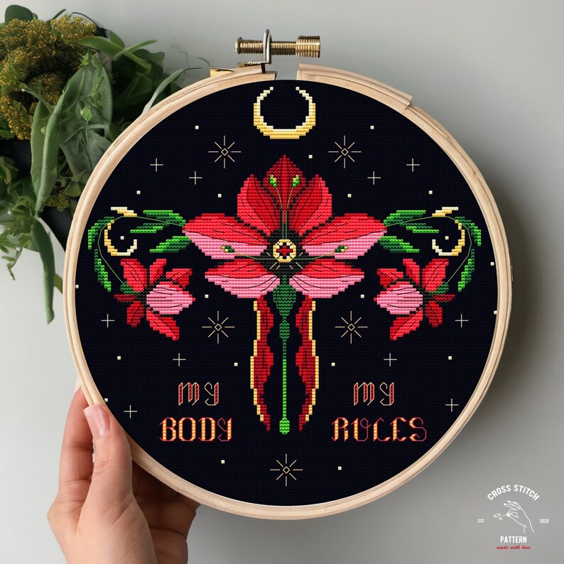 Puede incluir: Patr&oacute;n de punto de cruz con una flor estilizada con una luna creciente por encima. La flor es roja y rosa con hojas verdes. El texto "my body my rules" est&aacute; debajo de la flor.