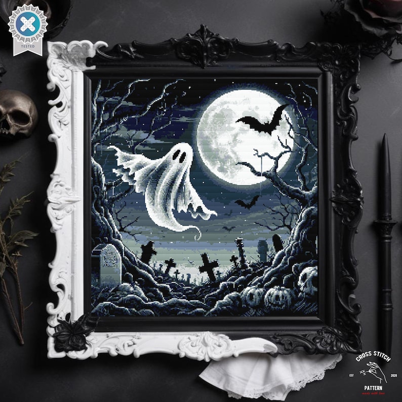 May include: A cross stitch pattern featuring a spooky Halloween scene with a white ghost flying in front of a full moon, bats, and a graveyard. The pattern is framed in a black and white ornate frame.