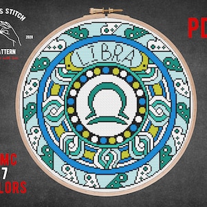May include: Cross stitch pattern for the zodiac sign Libra. The pattern features a blue, green, and yellow mandala design with the Libra symbol in the center. The pattern is available as a PDF download and requires 7 DMC colors.