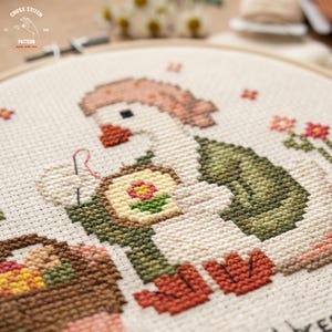 May include: Cross-stitch embroidery of a goose wearing a pink hat and green vest, holding a needle and thread. The goose is stitching a small framed flower. A basket of eggs is in the lower left. The text "CROSS STITCH" and "PATTERN" are in the upper left.