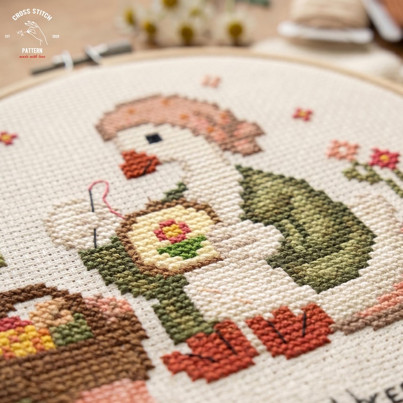 May include: Cross-stitch embroidery of a goose wearing a pink hat and green vest, holding a needle and thread. The goose is stitching a small framed flower. A basket of eggs is in the lower left. The text "CROSS STITCH" and "PATTERN" are in the upper left.