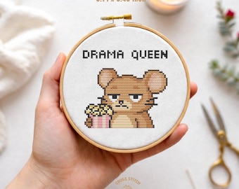 Pode incluir: Um mini bastidor de bordado com o texto "DRAMA QUEEN" acima de um rato de desenho animado segurando pipocas. O bastidor mede 9,42 x 8,71 cm. O rato tem uma expressão carrancuda.