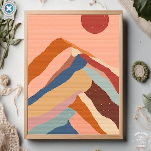 May include: A cross stitch pattern depicting a stylised mountain range with a large orange sun in the background. The mountain is made up of multiple layers of different colours, including orange, brown, pink, blue, and green.
