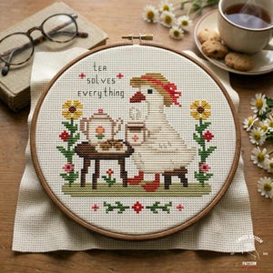 Puede incluir: Bordado de punto de cruz en un aro de madera con un ganso tomando té. El diseño incluye una tetera, flores y el texto "Tea Solves Everything". La paleta de colores incluye blanco, marrón, rojo, amarillo y verde.