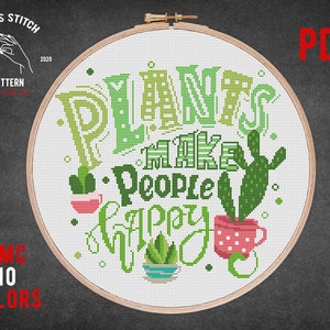 May include: A cross stitch pattern featuring a hoop with the text "Plants make people happy" in green and red lettering with a cactus and a potted plant design. The pattern is available as a PDF download and uses 10 colors.