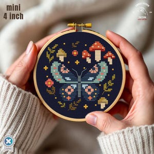 May include: A 4-inch mini cross-stitch embroidery hoop featuring a butterfly design with mushrooms and floral accents. The design is stitched on a dark blue fabric and set in a wooden hoop. The text "mini 4 inch" is visible.