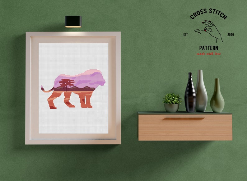 May include: A framed cross stitch pattern of a lion with a landscape inside its silhouette. The pattern is titled "Cross Stitch Pattern made with love" and includes the text "EST 2020".