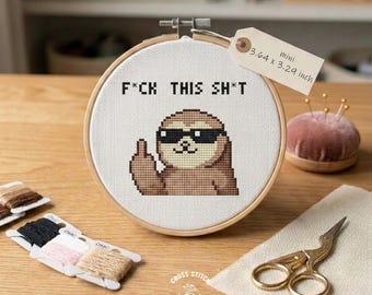 Pode incluir: Um mini bastidor de bordado em ponto cruz com o texto "F*CK THIS SH*T" e uma preguiça pixelizada usando óculos de sol e mostrando o dedo do meio. O bastidor mede 9,25 x 8,36 cm. Inclui fios DMC e tesouras douradas.