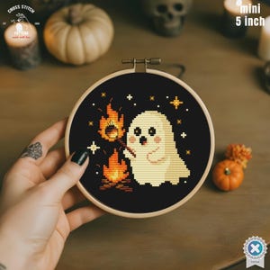 Könnte beinhalten: Ein Mini-Stickrahmen von 12,7 cm mit einem niedlichen Geist, der ein Marshmallow über einem Lagerfeuer röstet. Das Design ist vor einem schwarzen Hintergrund mit Sternen angeordnet. Der Rahmen ist in einem Holzrahmen gehalten.