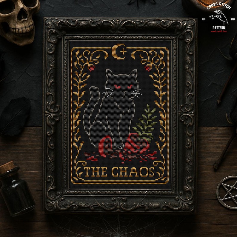 May include: Cross-stitch pattern featuring a black cat with red eyes, sitting on a red rose, framed in a decorative black frame. The text "THE CHAOS" is at the bottom. The frame is surrounded by gothic-themed objects.