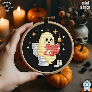 Może przedstawiać: Mini obręcz do haftu o średnicy 5 cali (12,7 cm) z motywem Halloween. Przedstawia ducha czytającego książkę z napisem "BOO" na toalecie. Tło jest czarne z gwiazdami i świecą.