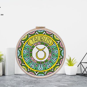 Peut inclure: Mod&egrave;le de point de croix pour le signe du zodiaque Taureau. Le motif repr&eacute;sente un symbole de taureau jaune entour&eacute; d'un mandala color&eacute; avec des accents verts, bleus, roses et jaunes.