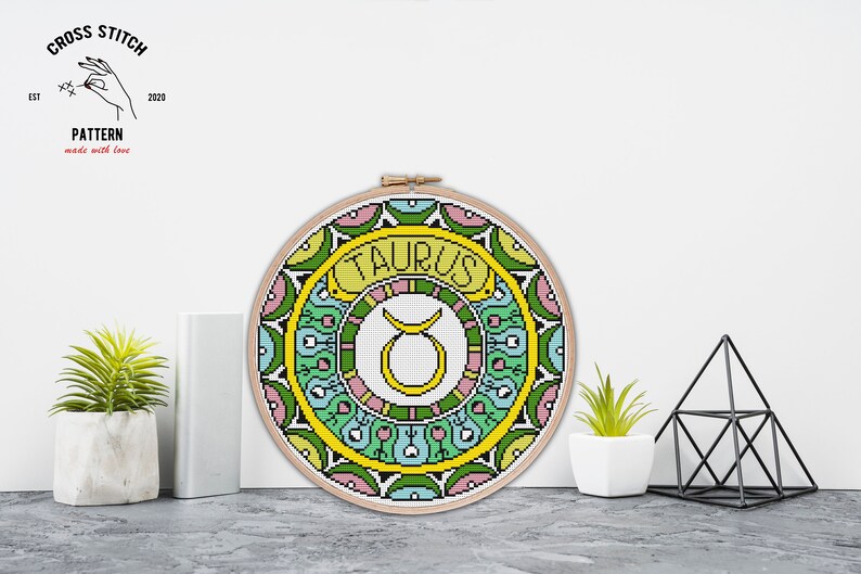 Peut inclure: Mod&egrave;le de point de croix pour le signe du zodiaque Taureau. Le motif repr&eacute;sente un symbole de taureau jaune entour&eacute; d'un mandala color&eacute; avec des accents verts, bleus, roses et jaunes.