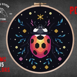May include: Cross stitch pattern featuring a colorful ladybug with black spots on a dark blue background with white stars and floral accents. The pattern is in a hoop and includes the text "Cross Stitch Pattern" and "DMC 15 Colors".