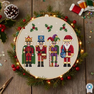 May include: A cross-stitch hoop featuring four festive nutcracker figures in red, green, and blue. The hoop is surrounded by a wreath of greenery, berries, and fairy lights. The text "CROSS STITCH PATTERN" is visible.