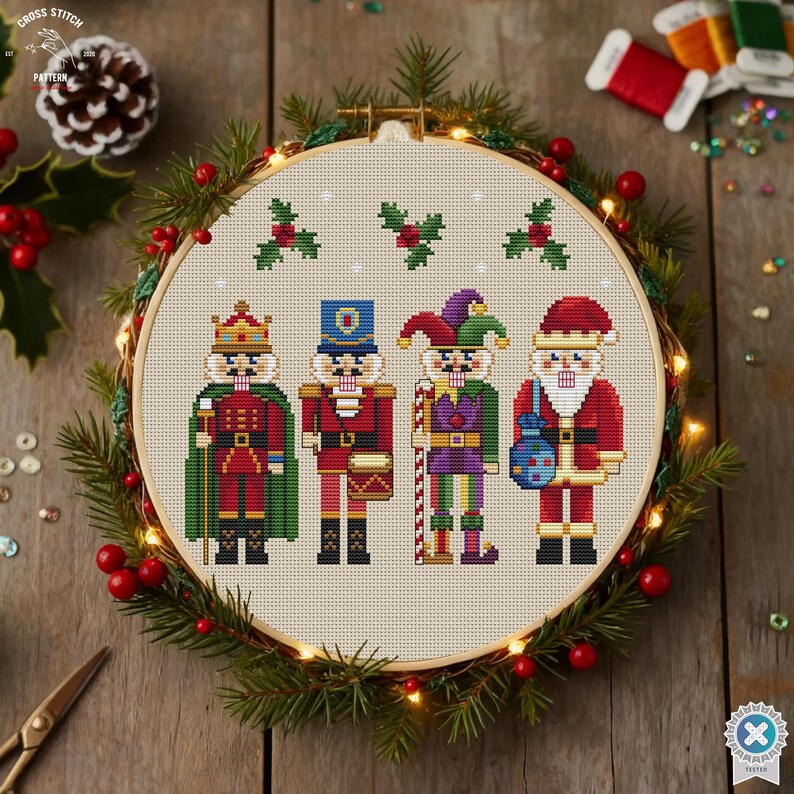 May include: A cross-stitch hoop featuring four festive nutcracker figures in red, green, and blue. The hoop is surrounded by a wreath of greenery, berries, and fairy lights. The text "CROSS STITCH PATTERN" is visible.