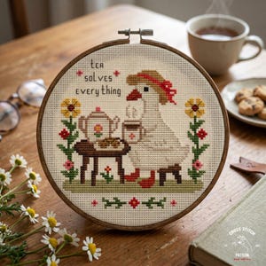 May include: A cross-stitch embroidery in a wooden hoop features a goose enjoying tea. The design includes a teapot, flowers, and the text "Tea Solves Everything." The color palette includes beige, brown, red, yellow, and green.
