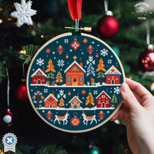 May include: A cross stitch pattern of a winter village scene with houses, trees, and reindeer. The pattern is in a hoop and is ready to be stitched.