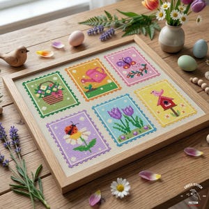 May include: A framed cross-stitch sampler featuring six colorful spring-themed designs. The designs include a basket of flowers, a watering can, a butterfly, tulips, a birdhouse, and a ladybug on a daisy. The sampler is in a light wood frame.
