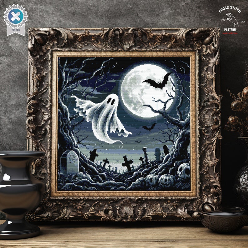 May include: A cross stitch pattern featuring a spooky Halloween scene with a white ghost flying in front of a full moon, bats, and a graveyard. The pattern is framed in a dark wood frame.