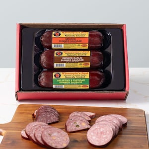 May include: A package of Wisconsin's Best summer sausage in a red box. The package contains three sausages: Smoked Summer Sausage, Smoked Garlic Summer Sausage, and Jalapeno & Cheddar Summer Sausage. Sliced sausage is on a wooden cutting board.
