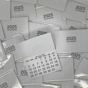 May include: A stack of white cards with the text "2025 Calendar" printed on them. One card has a January 2025 calendar printed on it.