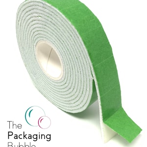 Op de afbeelding: Een rol groene schuimtape met een witte kleefrug. De tape is opgerold en het uiteinde van de tape steekt uit. De tape wordt gebruikt voor verpakking en afdichting.
