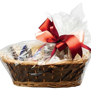 Puede incluir: Una cesta de mimbre llena de diversos artículos, envuelta en celofán transparente y atada con una cinta de satén roja. La cesta está decorada con un lazo de color melocotón.