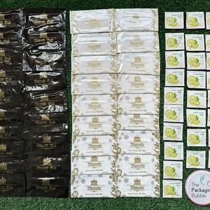 May include: A close-up of three stacks of individually wrapped wet wipes. The first stack is black and features the text "Majestic Oud". The second stack is white and features the text "Majestic Lemon Scented Wet Wipes". The third stack is white and features the text "Lemon Fresh Wipes".