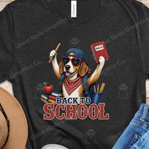 Könnte beinhalten: Ein dunkelgraues T-Shirt mit einer Grafik eines Beagle-Hundes, der eine blaue Baseballkappe, herzförmige Sonnenbrillen und ein rotes Bandana trägt. Der Hund hält einen Bleistift und ein rotes Buch mit der Aufschrift MATH. Text darunter: BACK TO SCHOOL.