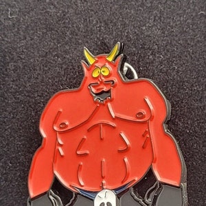 Könnte beinhalten: Rote Teufel-Anstecknadel mit Hörnern, einem Schädel und einem verschmitzten Grinsen. Die Anstecknadel ist aus Metall und hat ein schwarz-rotes Farbschema.
