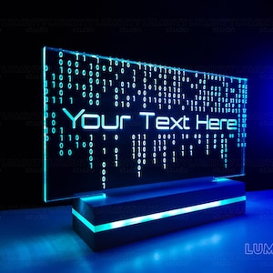 Può includere: Un cartello LED blu con sfondo bianco e il testo "Your Text Here" visualizzato in bianco. Il cartello è su una base nera con una striscia di luce LED blu.