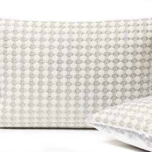 May include: Two white throw pillows with a silver geometric pattern. The pillow on the left has a more textured fabric, while the pillow on the right has a smooth, velvet-like fabric.
