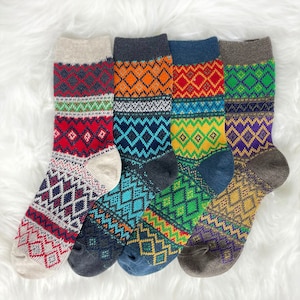 May include: Five pairs of colorful patterned socks. Each sock features a unique design with geometric patterns in shades of red, orange, blue, green, and purple. The socks have a soft, textured appearance, perfect for cold weather.