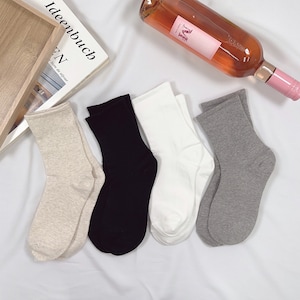 May include: Four pairs of ankle socks in beige, black, white, and gray. The socks are folded and laid out on a white surface.