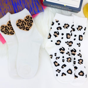 May include: Two pairs of white socks with a leopard print design. One pair has a heart-shaped leopard print design on the front.