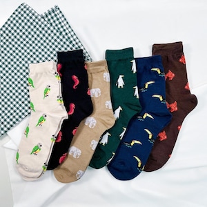 May include: A collection of six colorful socks with various animal patterns. Designs include parrots, seahorses, elephants, penguins, toucans, and fish. The socks are arranged on a white surface with a green and white checkered cloth in the background.