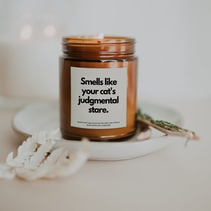 May include: A brown glass candle jar with a white label that reads "Smells like your cat's judgmental stare."  Hand-poured, vegan coconut soy wax with a burn time of 30 hours. Made with love & sarcasm.