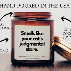 May include: A brown glass candle jar with a white label that reads "Smells like your cat's judgmental stare." The candle is hand-poured in the USA with undyed coconut soy wax and a natural cotton wick. It is non-toxic and has a burn time of 50 hours.