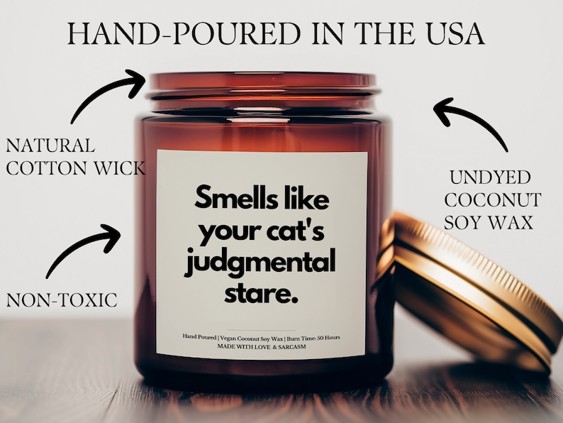 May include: A brown glass candle jar with a white label that reads "Smells like your cat's judgmental stare." The candle is hand-poured in the USA with undyed coconut soy wax and a natural cotton wick. It is non-toxic and has a burn time of 50 hours.