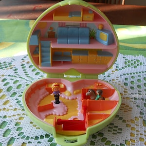 May include: A green and pink plastic toy house with a horse stable and two figures. The house is open and shows a kitchen, living room, and bedroom. The stable has a horse and a rider.