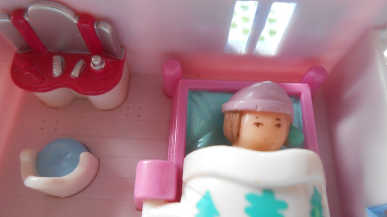 Puede incluir: Un juego de casa de mu&ntilde;ecas rosa y blanco con una mu&ntilde;eca con un sombrero rosa y una manta blanca acostada en una cama. La casa de mu&ntilde;ecas tambi&eacute;n cuenta con un tocador con un espejo y una silla peque&ntilde;a.