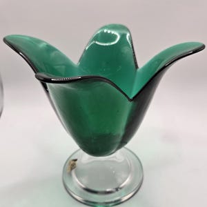 May include: A green glass vase with a flower-shaped top and a clear glass base.