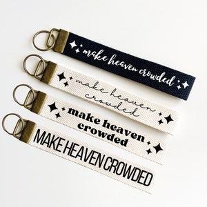 Peut inclure: Quatre porte-clés avec l'inscription "Make Heaven Crowded" imprimée dessus. Les porte-clés sont en tissu blanc et noir avec des anneaux en métal doré. L'inscription est imprimée en lettres noires et blanches.