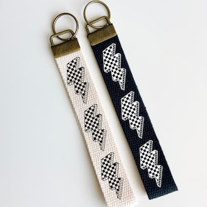 Peut inclure: Deux porte-clés avec des motifs d'éclairs en damier noir et blanc. Un porte-clés est sur une sangle noire et l'autre sur une sangle crème.